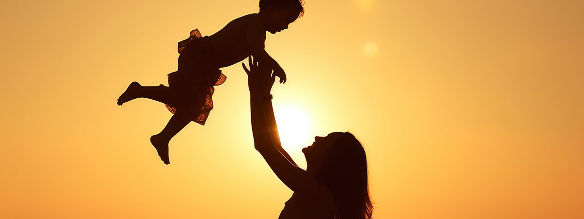 Silueta de madre alzando a su hijo/hija contra un atardecer dorado sobre el mar