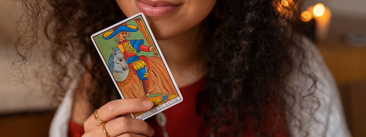 Mujer joven con cabello rizado sosteniendo una carta del Tarot Rider Waite frente a su rostro