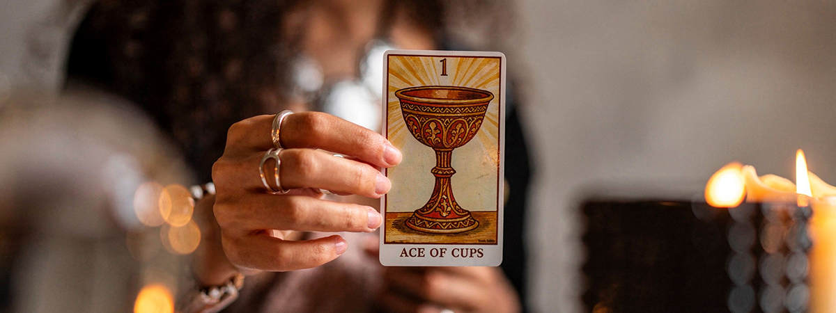Manos de mujer sosteniendo el As de Copas del Tarot Rider Waite sobre una mesa con velas encendidas