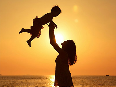 Silueta de madre alzando a su hijo/hija contra un atardecer dorado sobre el mar