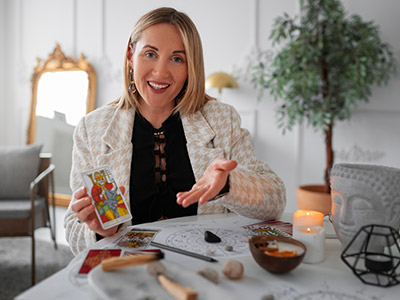 Lectora de tarot sonriendo con carta del Hierofante frente a cartas y materiales esotéricos sobre mesa blanca